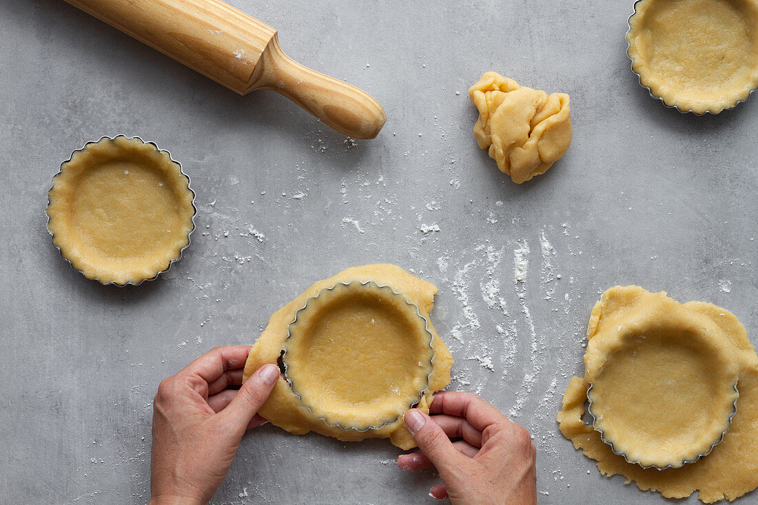 Top view of crop anonymous housewife filling metal forms with shortcrust pastry dough while preparing lemon pie in kitchen