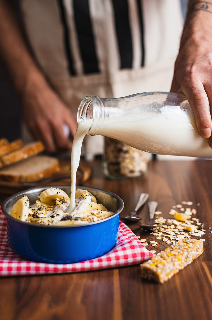 Joghurt aus Glasflasche in eine Schale mit Müsli und Banane giessen