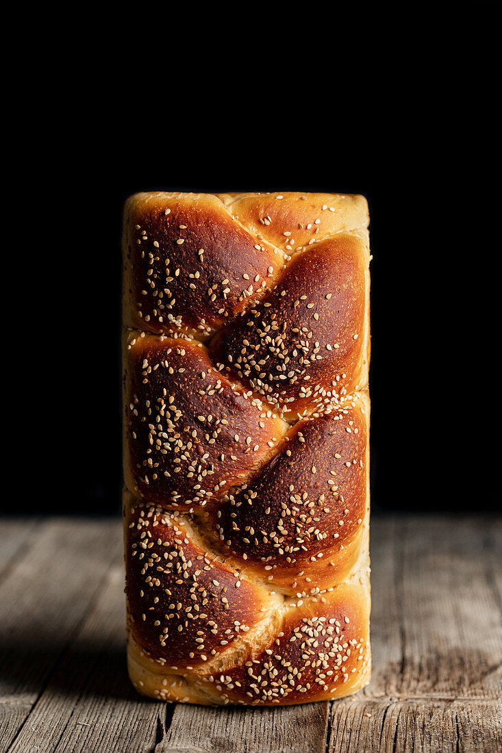 Loaf of fresh bread with sesame placed on cutting board in kitchen on black background