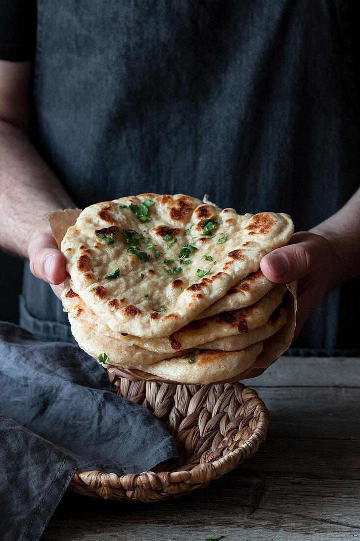 Unrecognizable male baker in apron with traditional Naan bread garnished with herbs