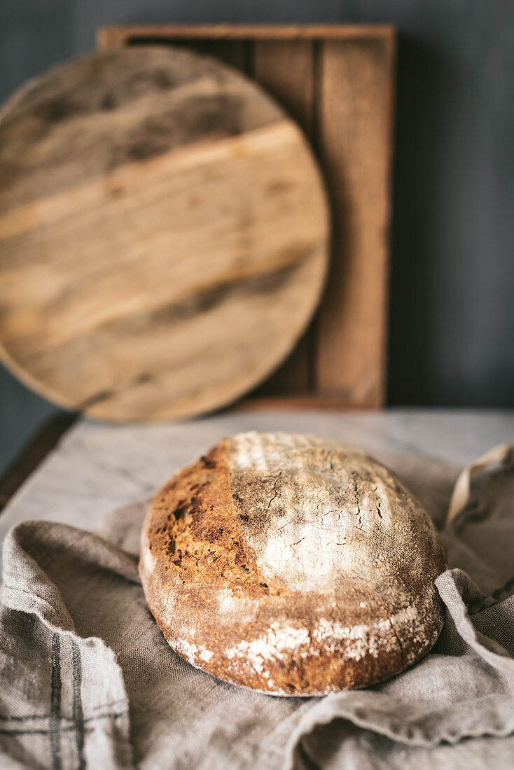 Round loaf of delicious homemade bread placed on piece of cloth on table in kitchen