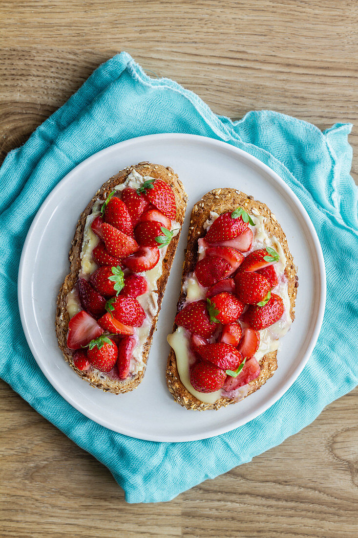 Yummy sweet bread toasts with fresh chopped strawberries and honey served on plate on blue tablecloth
