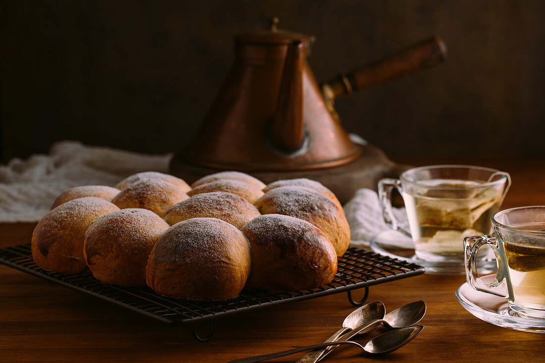 Identical appetizing buns with round shape and golden surface decorated with sugar powder on metal cooling rack on wooden table