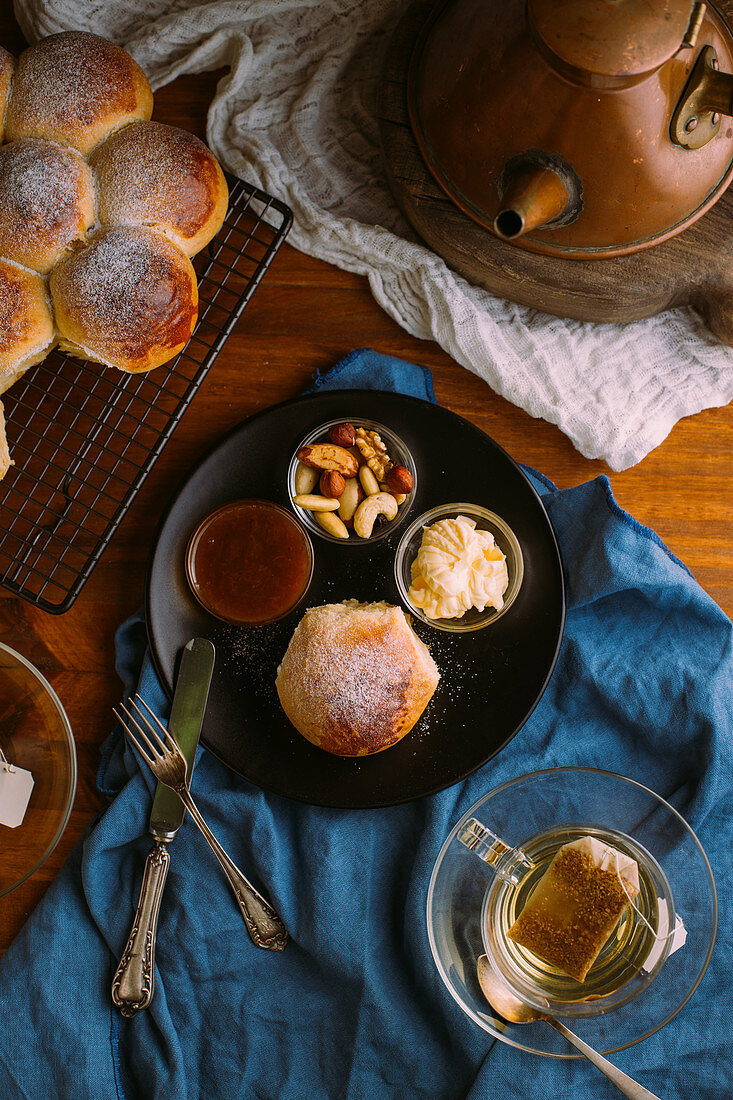 Frisch gebackenes, süßes Brötchen, Nüsse, Marmelade und Butter auf Teller