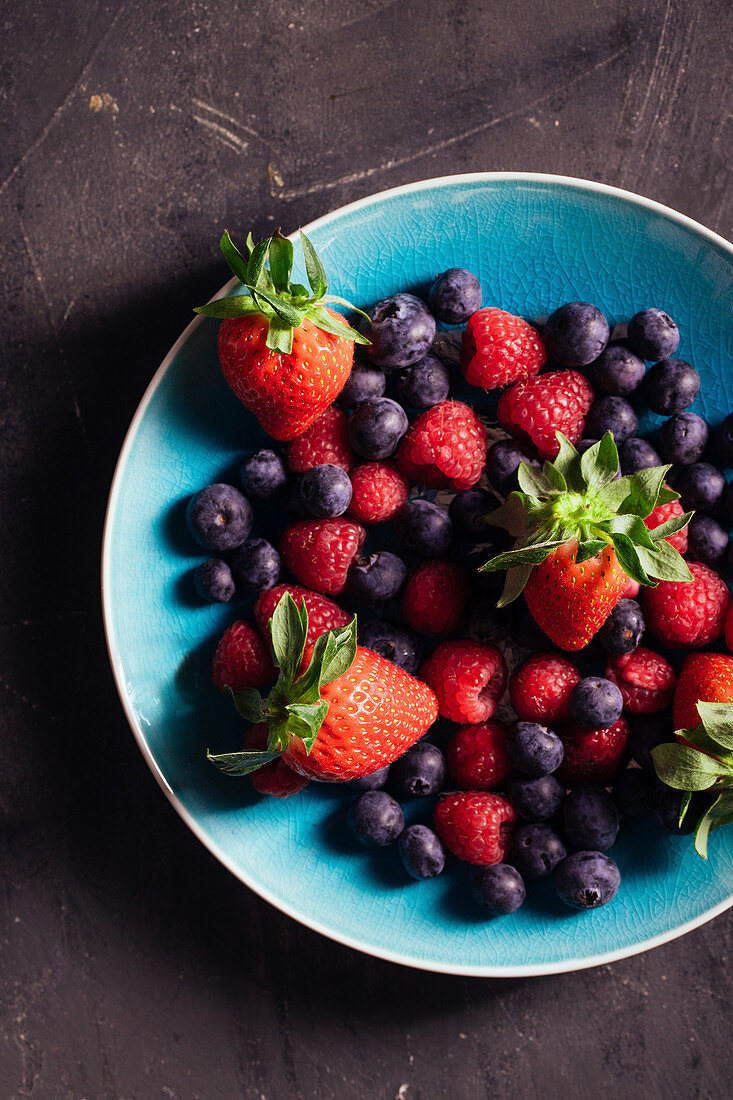 Frische Erdbeeren, Blaubeeren und Himbeeren in blauer Schale