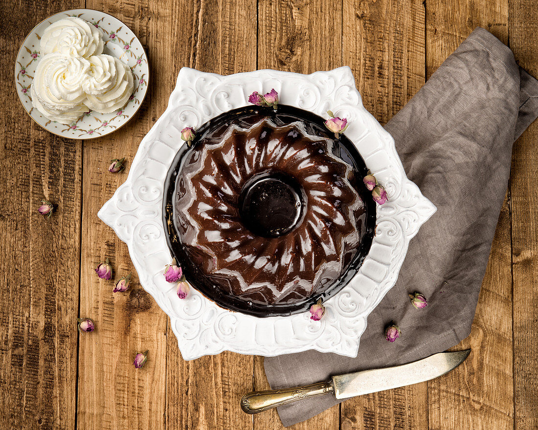 Chocolate bundt cake with cream served on white ceramic plate on wooden surface