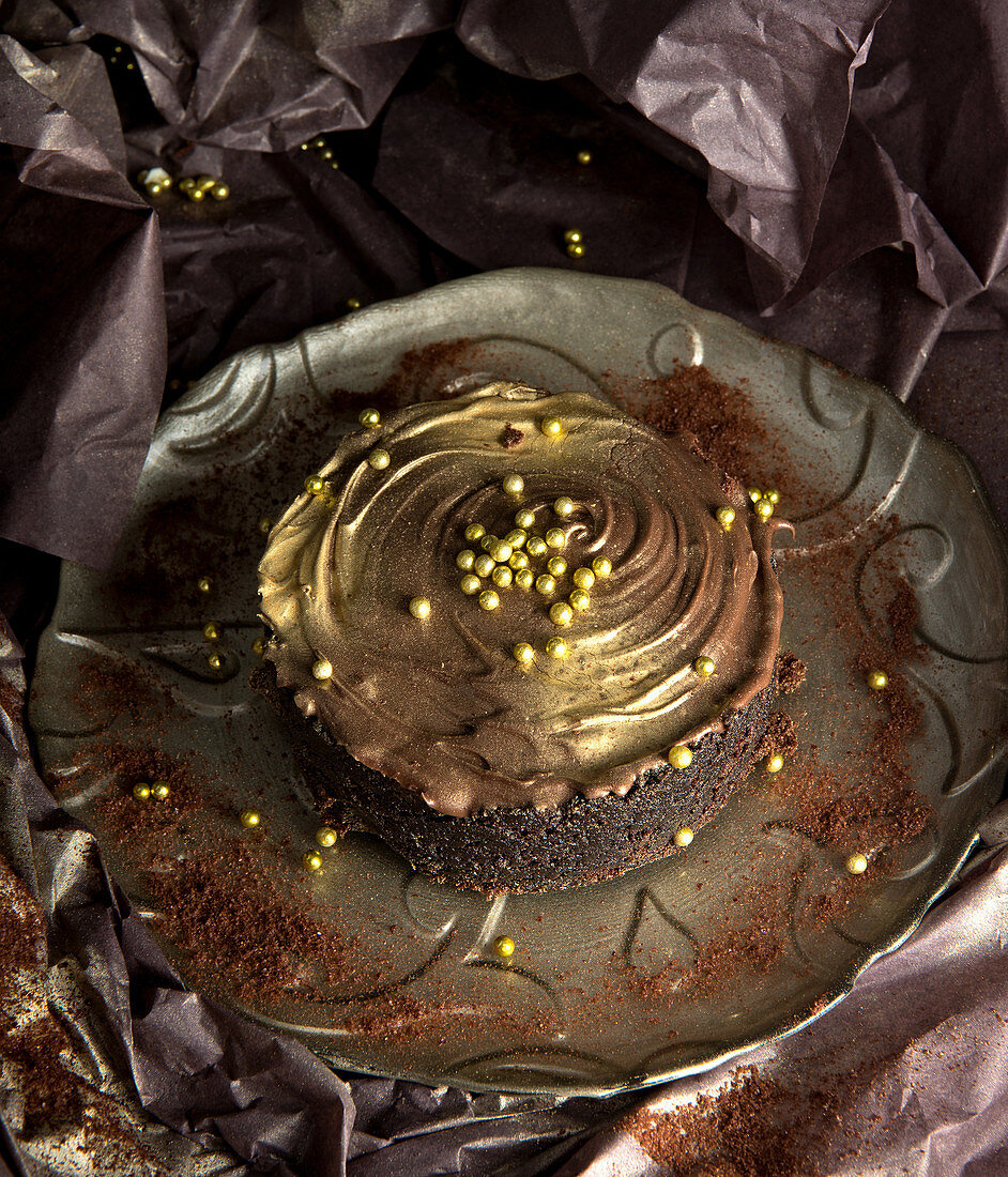 Chocolate cake with cream and golden chips placed against shabby background