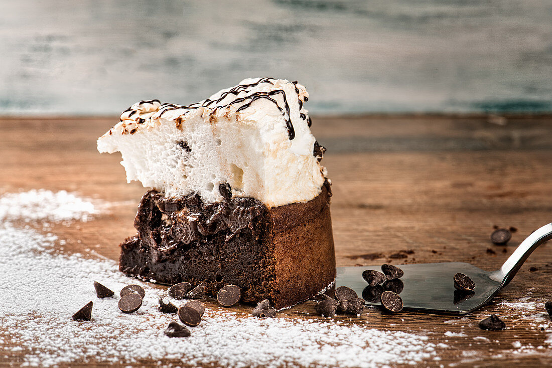 Chocolate cake with meringue placed on wooden table against shabby background