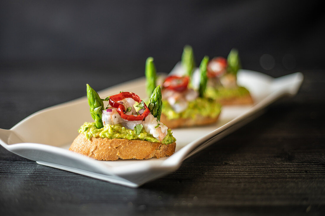 Small sandwiches with shrimp and vegetables placed on ceramic plate on black table in cafe