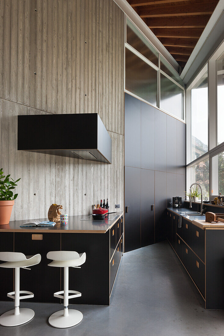 Modern kitchen with concrete wall, black cabinets and white bar stools