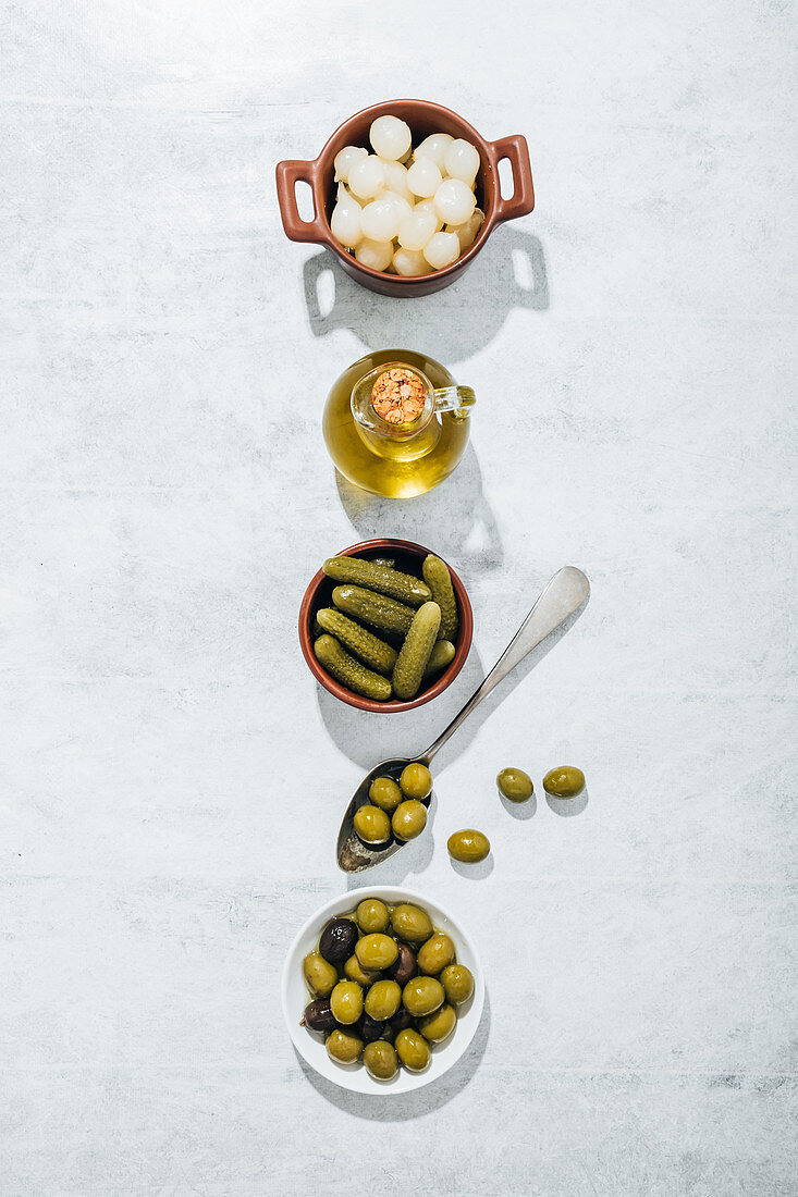 Bowl with pickled cucumbers and plate with olives placed on table in row along with glass oil jug