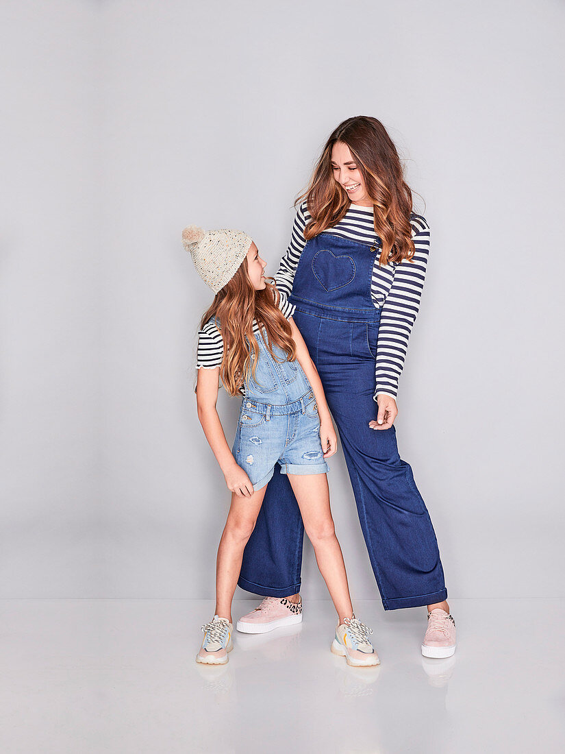 A mother and daughter wearing similar outfits (denim dungarees and striped tops)