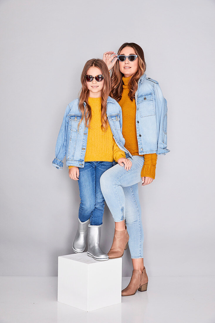 A mother and daughter wearing similar outfits (denim jackets, mustard-yellow jumpers and jeans)
