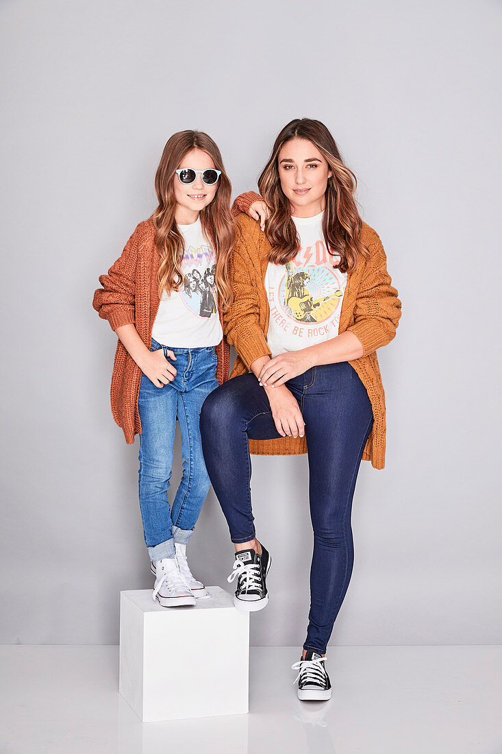 A mother and daughter wearing similar outfits (brown jackets, t-shirts and jeans)