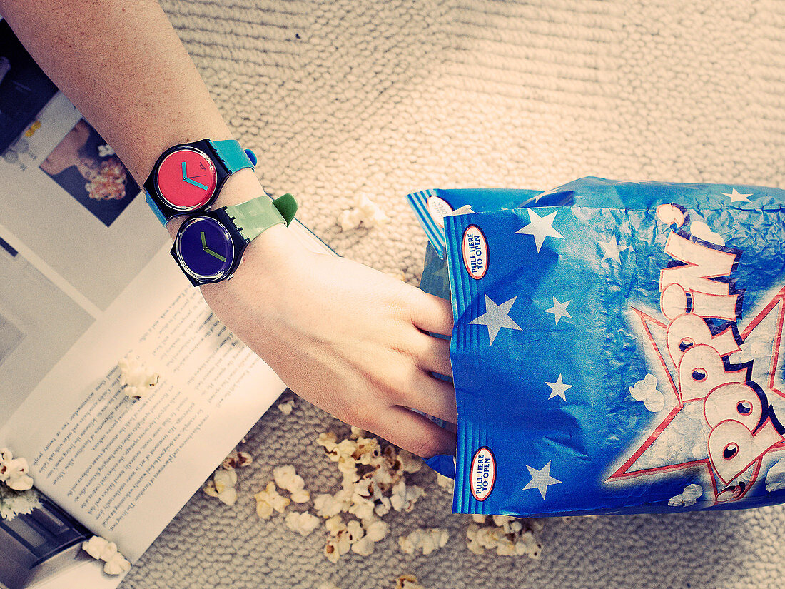 A woman's hand with two wristwatches taking popcorn from a bag