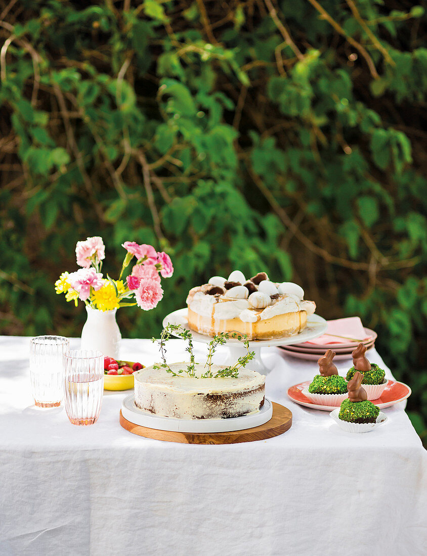 Kuchen und Gebäck fürs Osterfest auf gedecktem Tisch im Garten