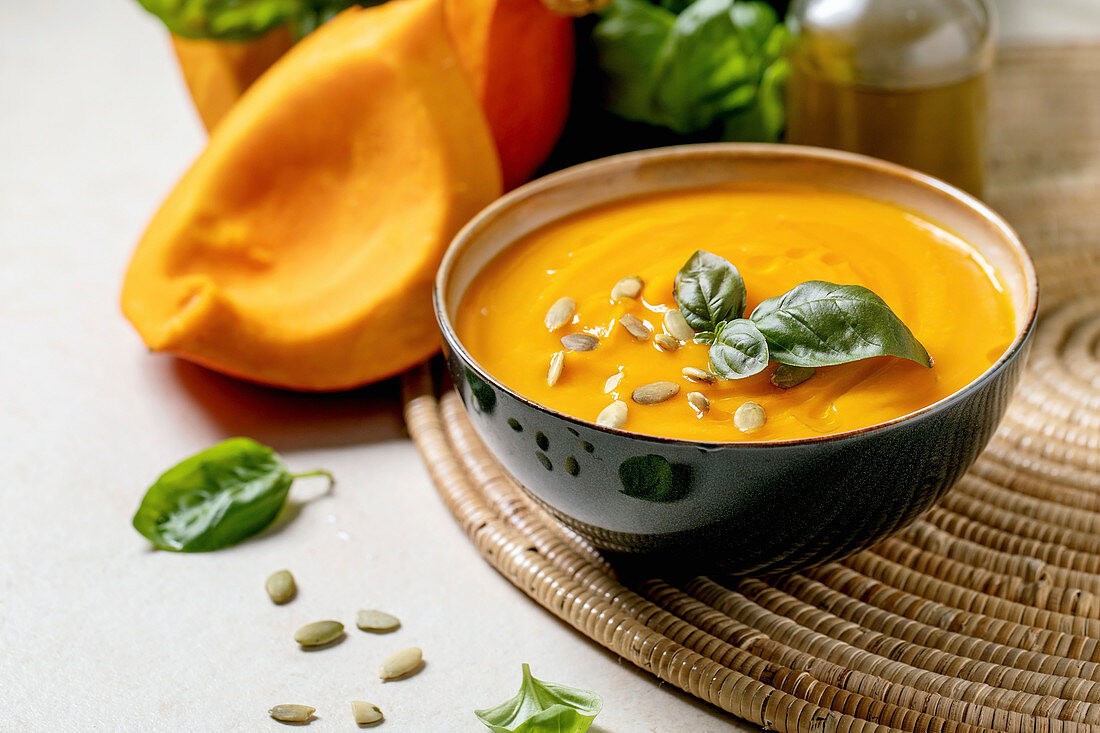 Bowl of pumpkin vegetarian cream soup decorated by fresh basil, olive oil and pumpkin seeds