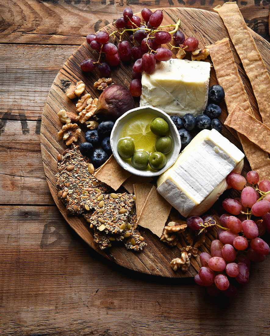 Käse mit Crackern, Früchten und Oliven auf Holzbrett