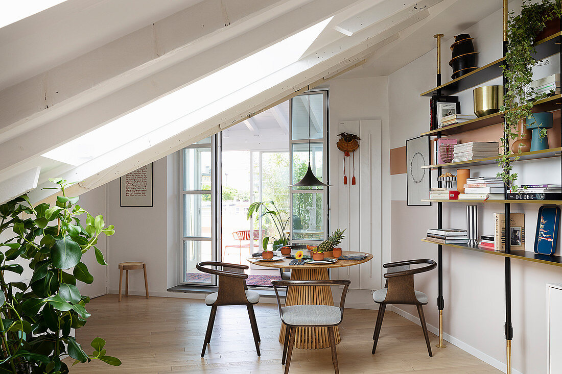 A round table with designer chairs and an open shelf in an attic room