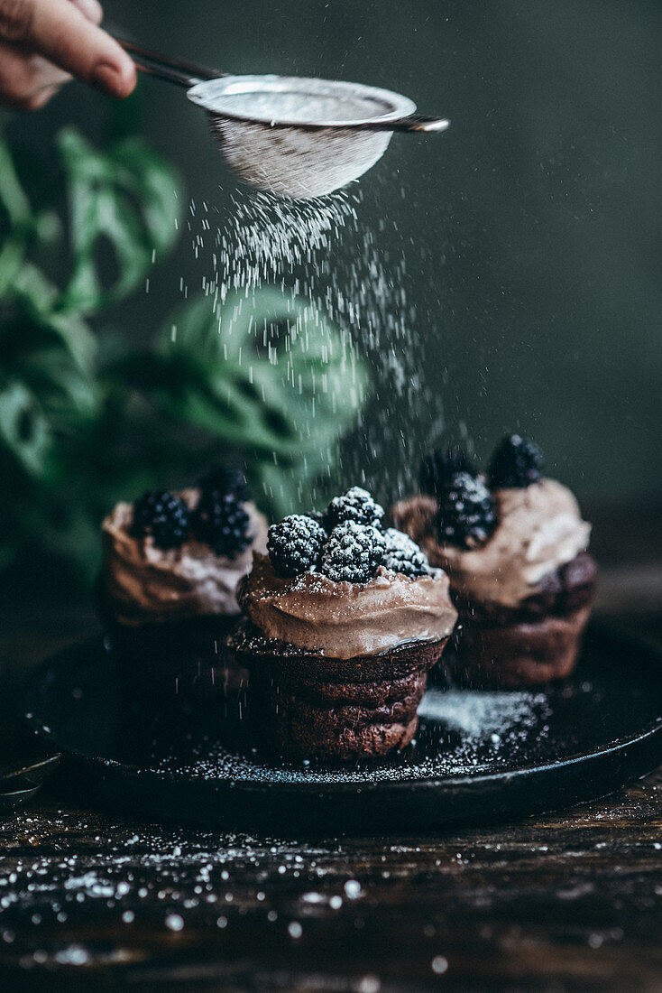 Chocolate cupcakes with coffee cream and blackberries sprinkled with powdered sugar