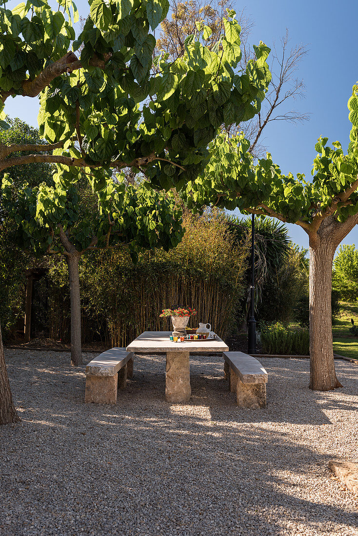 A shady gravel area with a stone table and benches