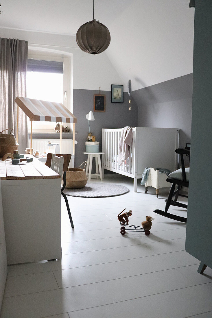 Nursery decorated in shades of grey with cot against knee wall