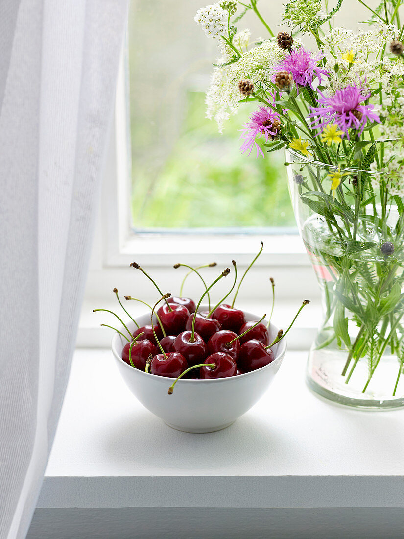 A bowl of cherries on a windowsill