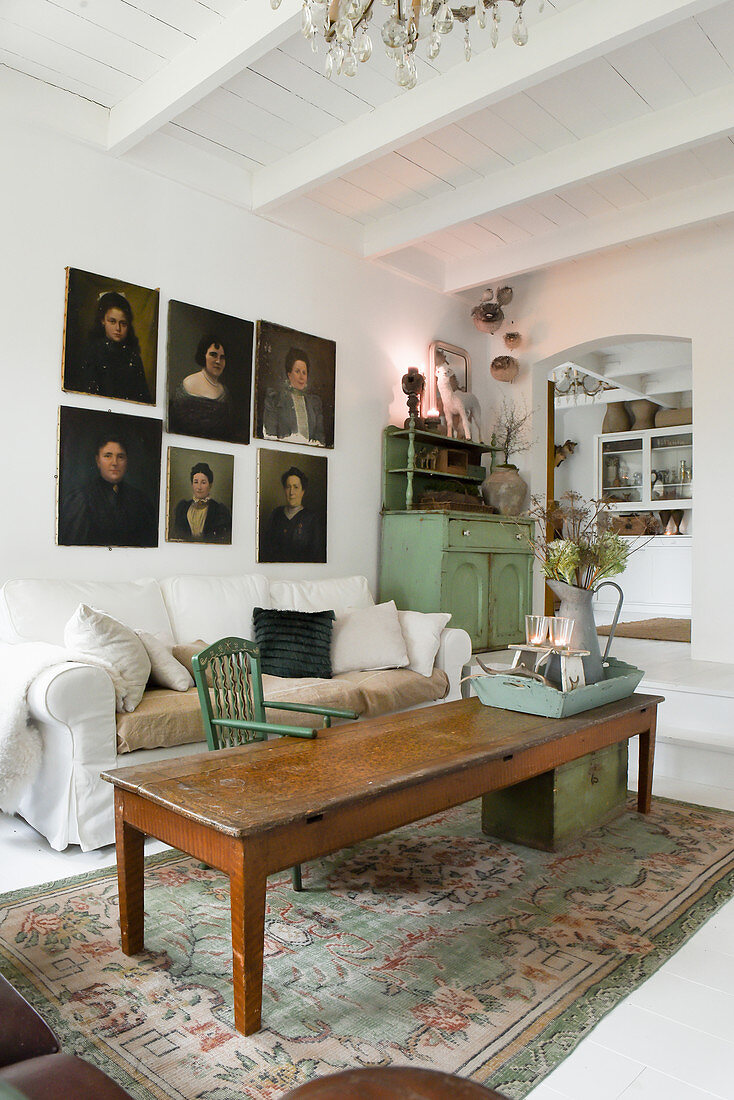 An old wooden table, a light covered sofa and a portrait painting in a living room