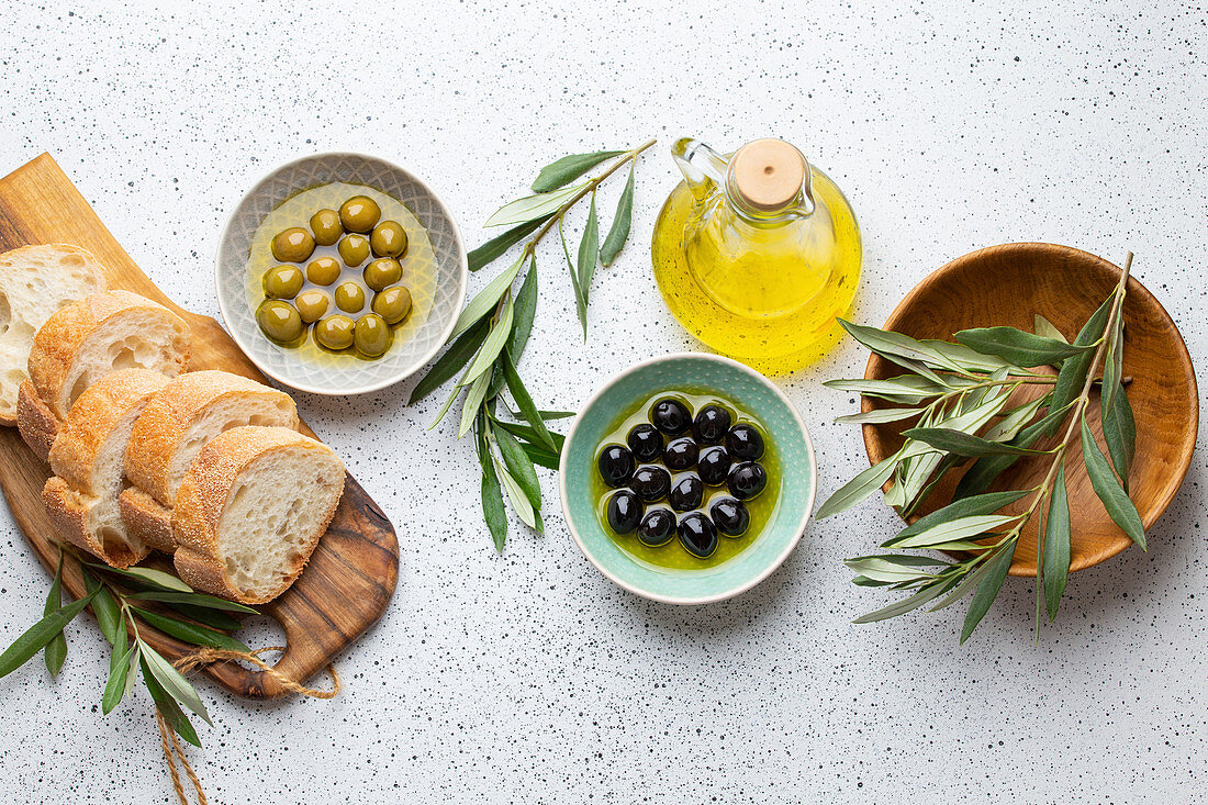 Green and black olives with olive oil in a glass bottle, olive tree sprigs and cut fresh ciabatta bread