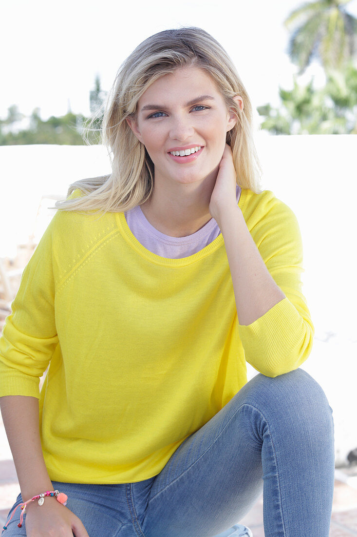 A young blonde woman wearing a yellow jumper and jeans