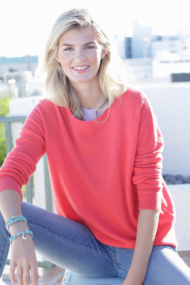 A young blonde woman wearing a coral-coloured turtle-neck jumper