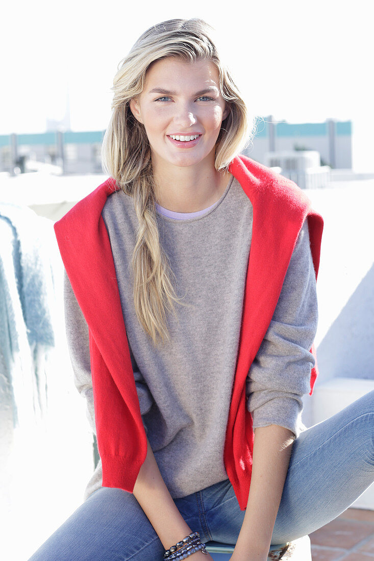 A young blonde woman wearing a light-coloured jumper with a coral-coloured jumper over her shoulders