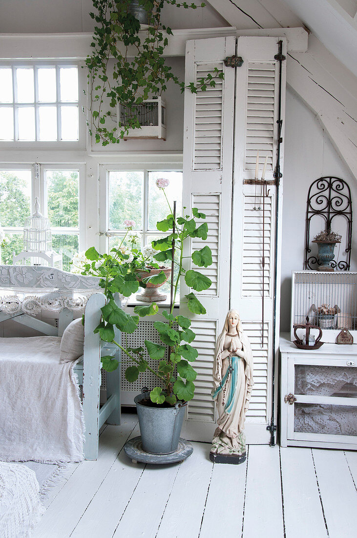 A statue of Mary and a pot plant in front of cupboard with louvre doors in a white, shabby-chic style living room