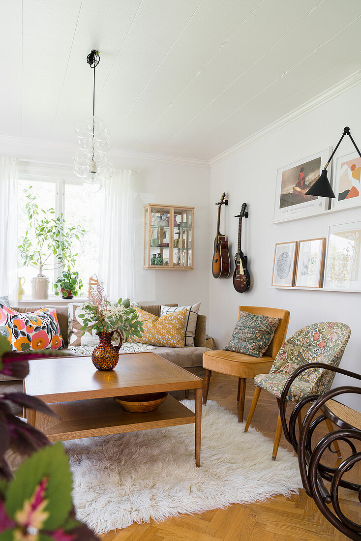 Coffee table on flokati rug, retro armchairs and sofa with scatter cushions in living room