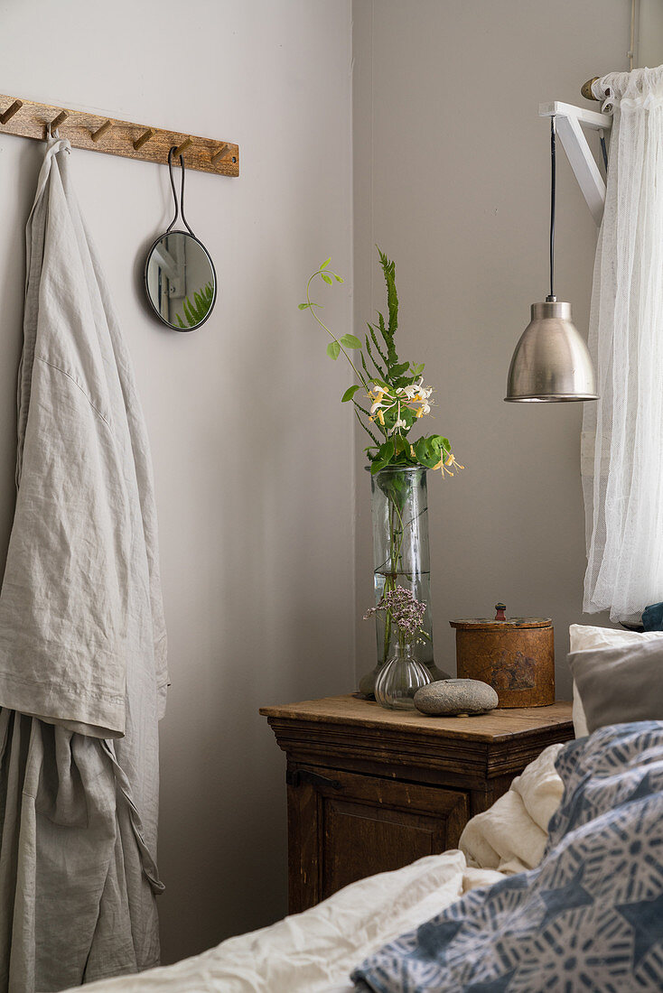 A bedside table next to a bed and a row of hooks in a rural bedroom
