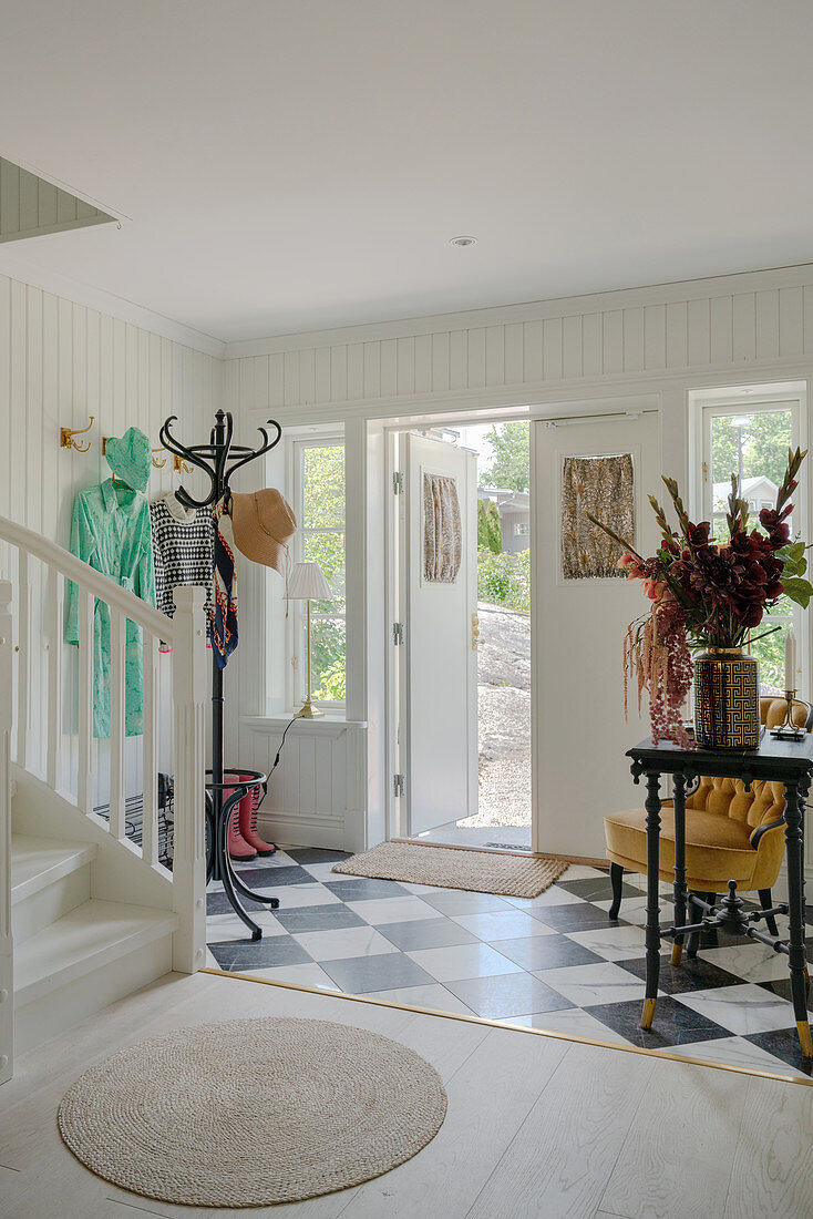 An entrance area with white wood panelling, and a black-and-white tiled floor