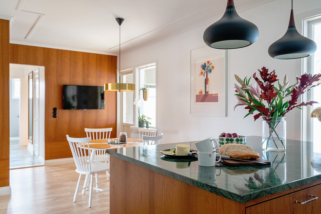 A kitchen island with a green marble worktop and a dining area in the background