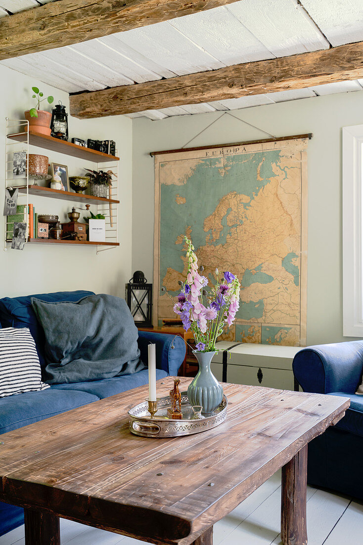 A rustic coffee table, a sofa with a blue cover and a map of Europe in a rural-style living room