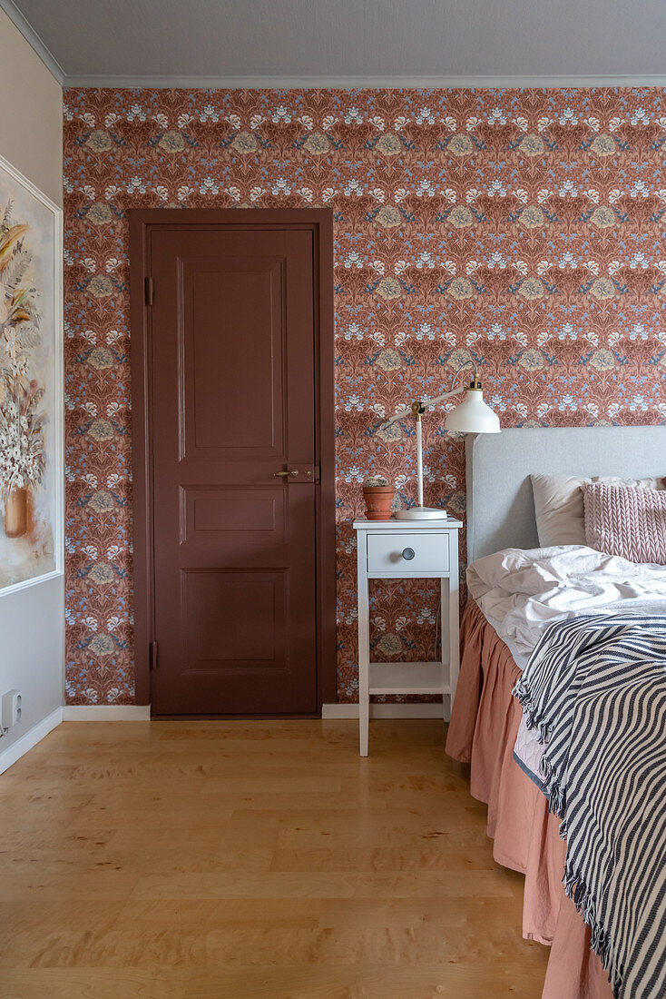 A door next to a double bed in a wallpapered bedroom