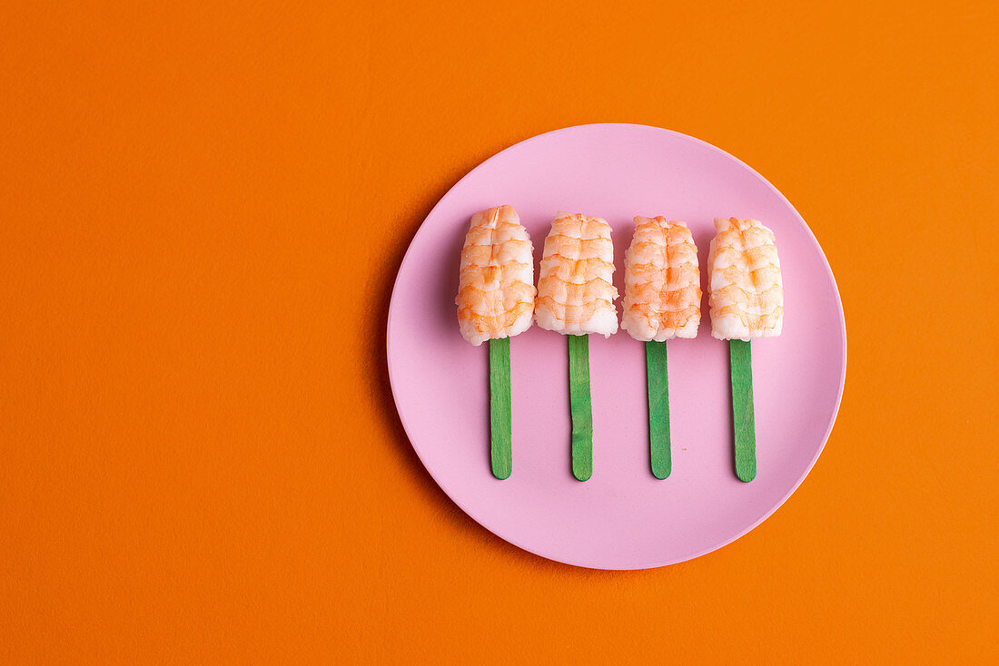 Top view of palatable set of Ebi Nigiri sushi with prawns served in shape of popsicle and placed on plate on orange background in studio