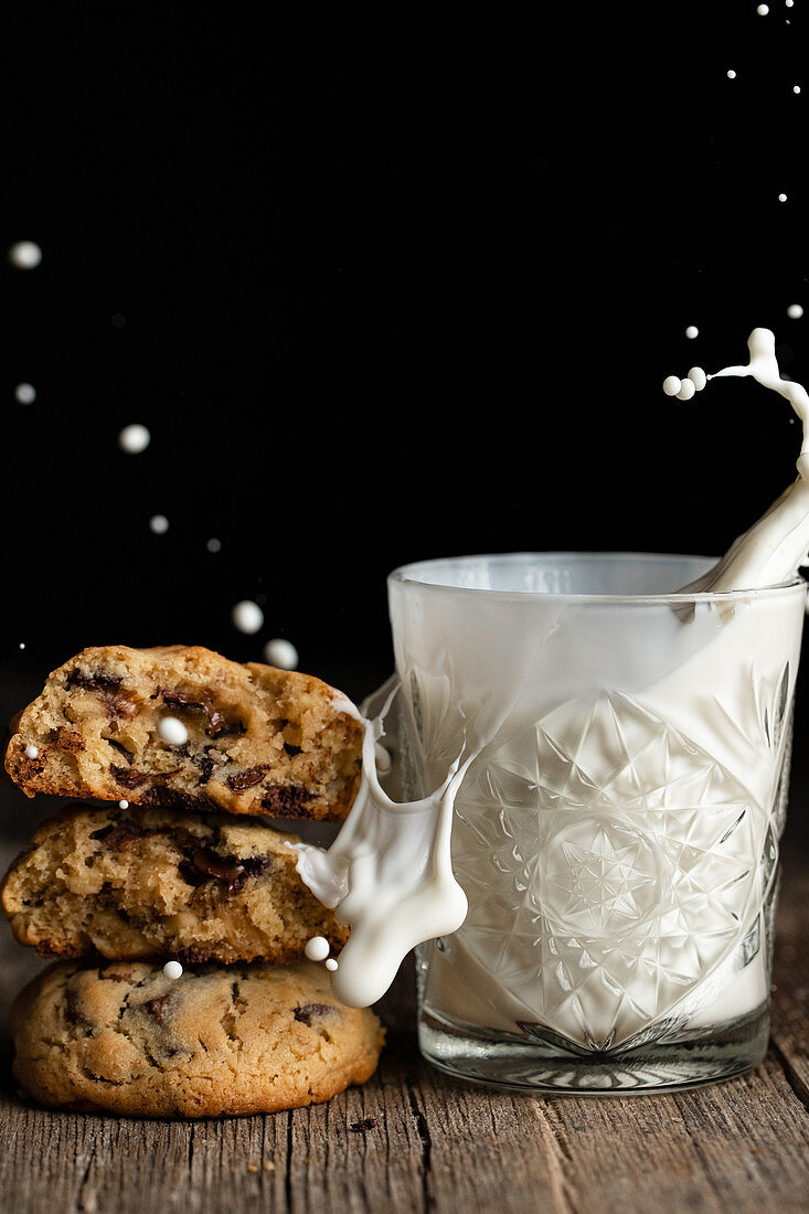 Gestapelte Chocolatechip Cookies neben Glas mit Milchsplash
