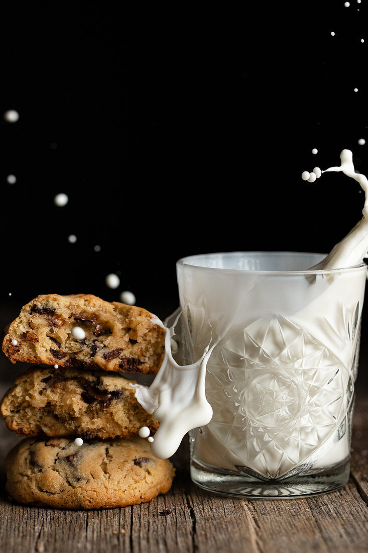 Pile of tasty chocolate cookies placed on wooden table near glass with splashing milk