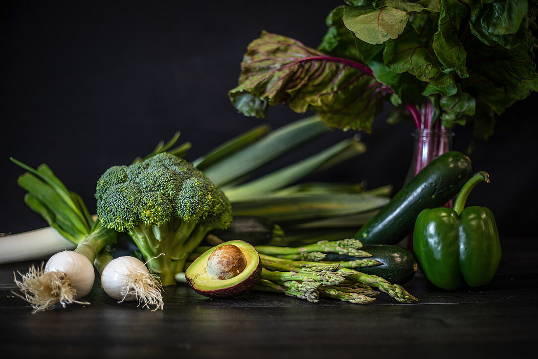 Bunch of various green vegetables placed on dark wooden table on black background