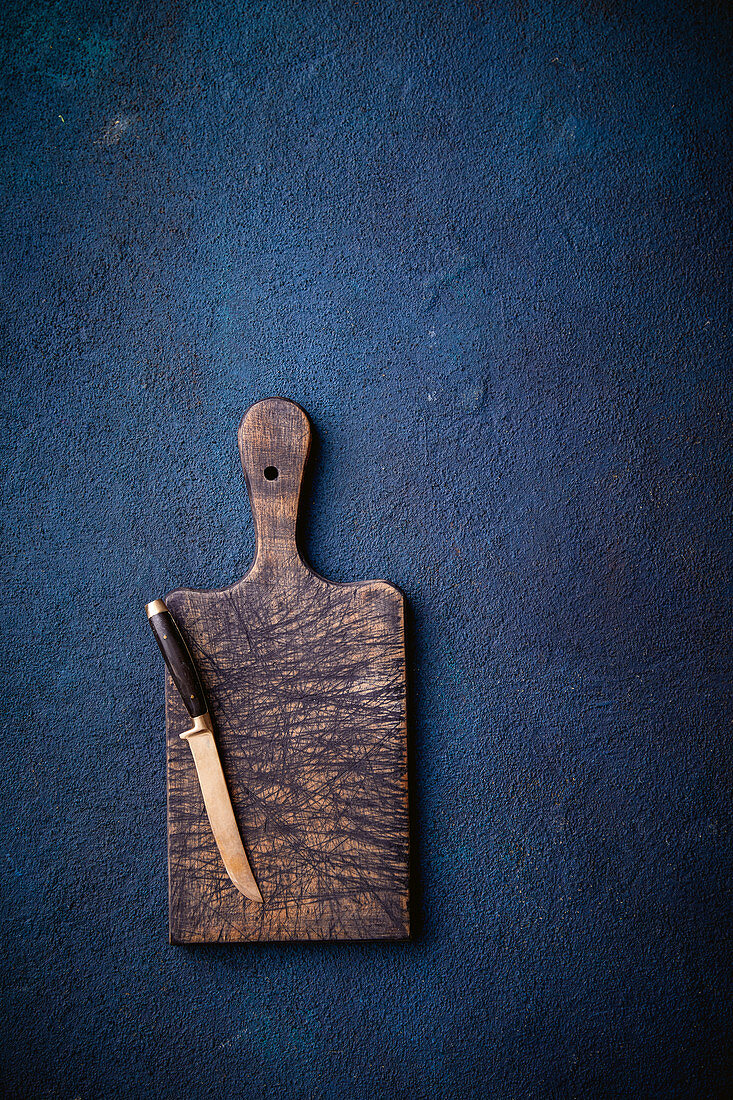 A wooden chopping board with a knife on a blue surface