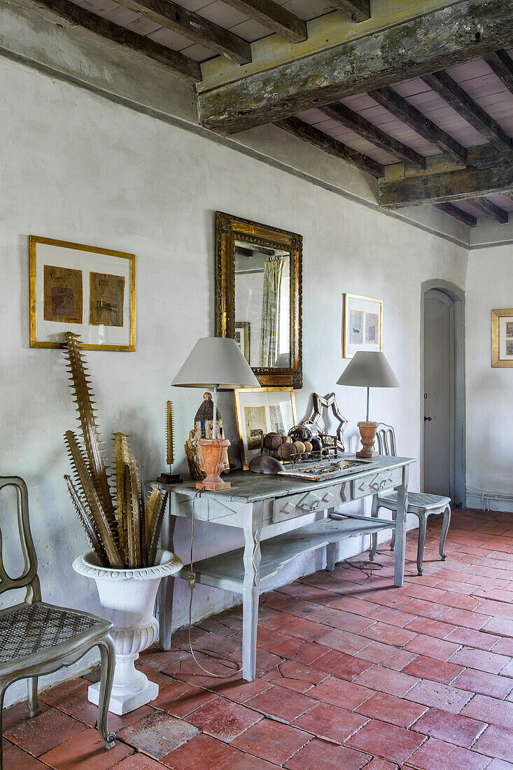 Console table with lamps in room with terracotta floor tiles and wood-beamed ceiling