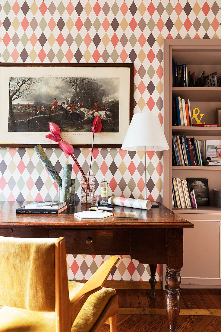 An antique desk in front of a wall with diamond-patterned wallpaper