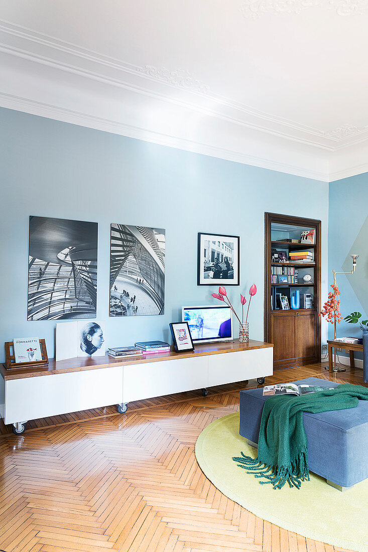Schwarz-weiße Fotos an blauer Wand über Lowboard in Altbau-Wohnzimmer mit Parkettboden