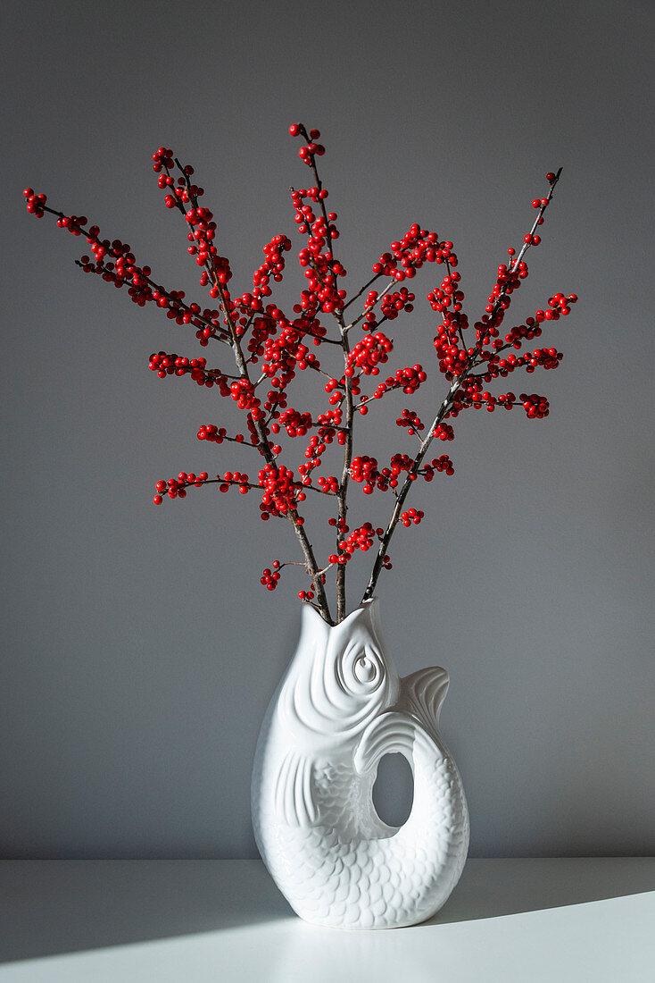 Branches of winterberry berries in fish-shaped vase