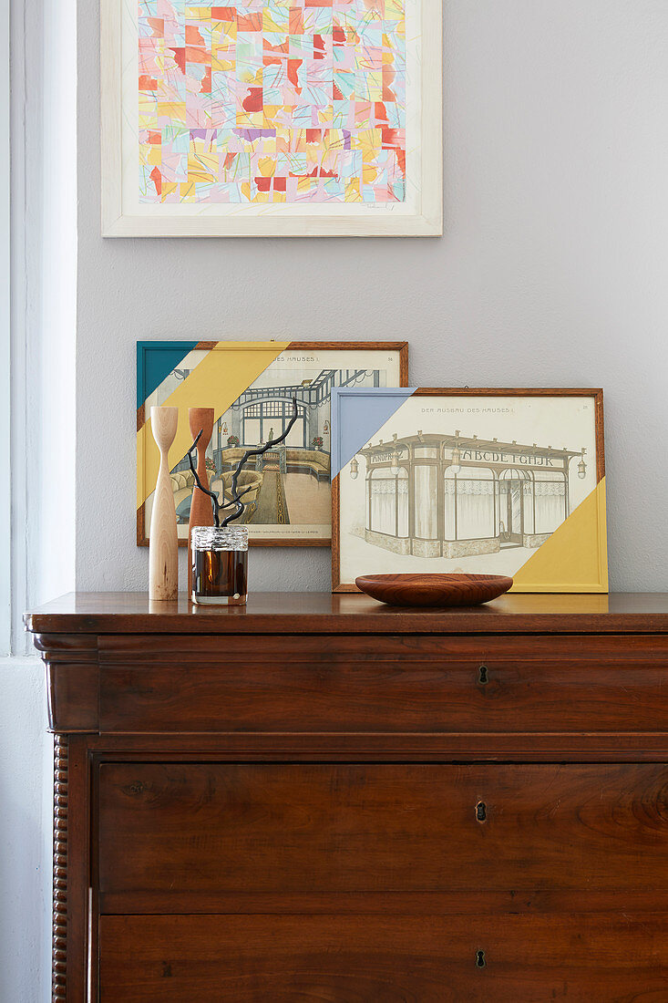 Arrangement of old pictures and frames partially painted over on top of chest of drawers