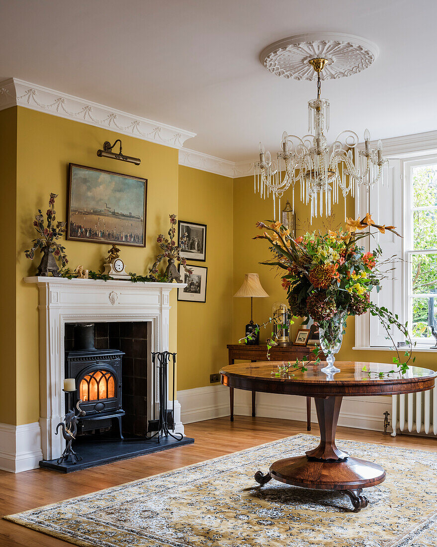 Woodburning stove in fireplace of Regency entrance hallway with polished wooden table and chandelier